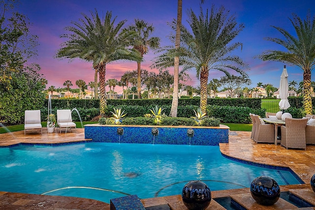 pool at dusk with pool water feature and a patio area