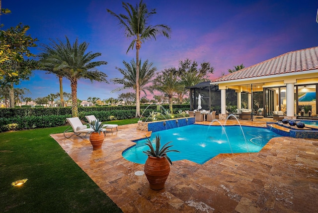 pool at dusk featuring a patio, pool water feature, and a hot tub