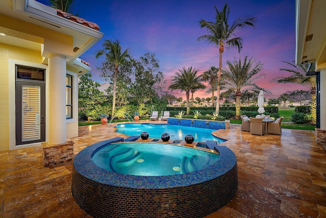 pool at dusk featuring an in ground hot tub, pool water feature, and a patio