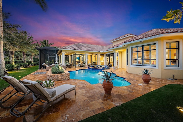 pool at dusk featuring a sunroom, an in ground hot tub, pool water feature, and a patio