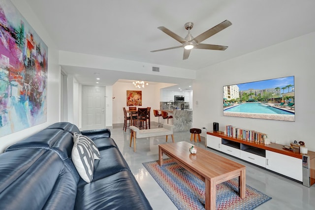 living room with ceiling fan with notable chandelier and concrete floors