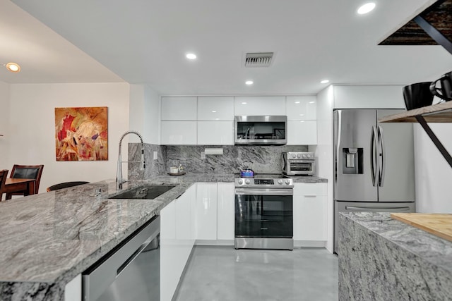 kitchen with appliances with stainless steel finishes, white cabinetry, sink, backsplash, and light stone counters