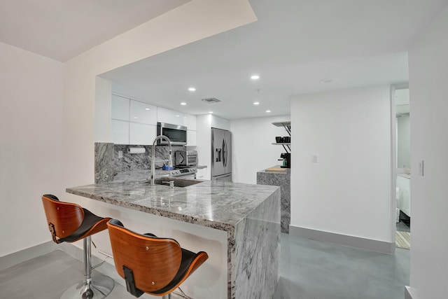 kitchen with a breakfast bar, sink, white cabinetry, appliances with stainless steel finishes, and kitchen peninsula