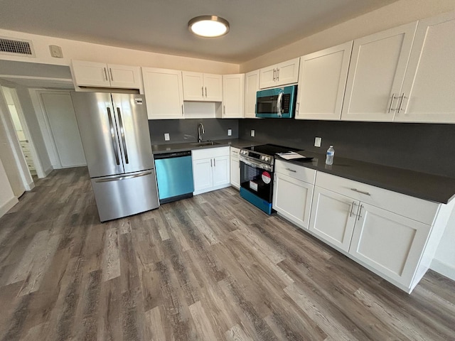 kitchen with white cabinets, appliances with stainless steel finishes, dark hardwood / wood-style flooring, and backsplash