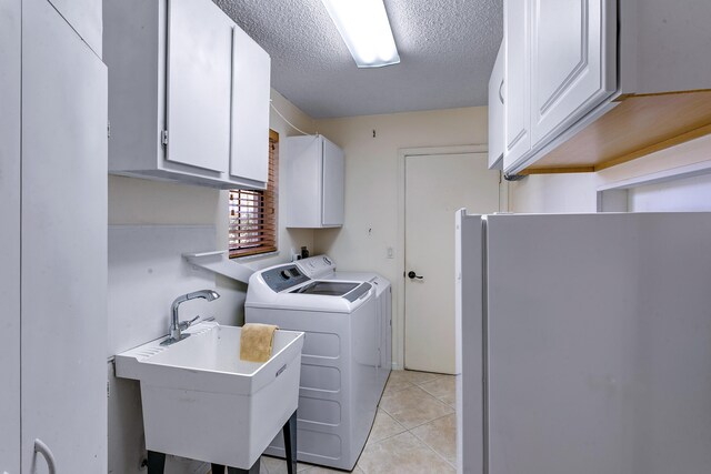 laundry area featuring light tile patterned flooring, sink, cabinets, a textured ceiling, and washer and clothes dryer