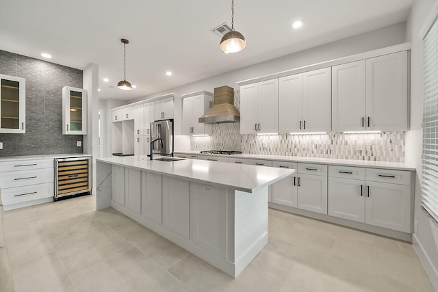 kitchen with white cabinetry, wine cooler, pendant lighting, a center island with sink, and custom exhaust hood