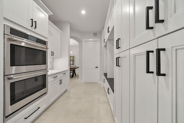 kitchen featuring white cabinets, stainless steel double oven, light tile patterned floors, and tasteful backsplash