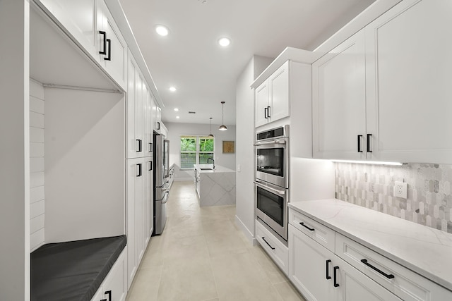 kitchen featuring decorative backsplash, light stone countertops, decorative light fixtures, white cabinetry, and stainless steel appliances