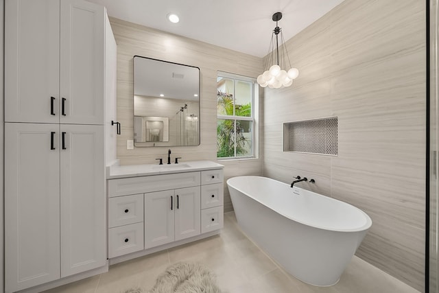 bathroom with a tub to relax in, tile patterned floors, vanity, and tile walls