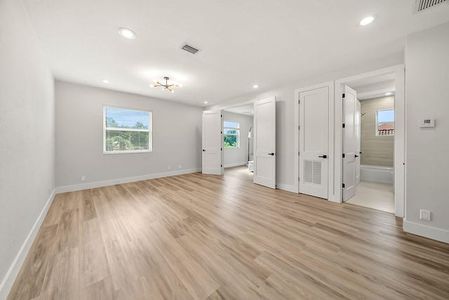 spare room featuring a chandelier, light hardwood / wood-style flooring, and a healthy amount of sunlight