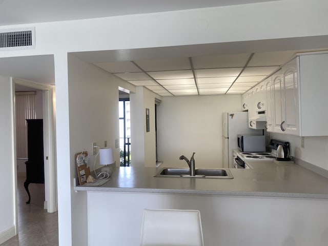 kitchen featuring kitchen peninsula, a paneled ceiling, electric stove, sink, and white cabinetry