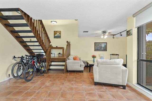 tiled living room featuring ceiling fan, rail lighting, and a textured ceiling