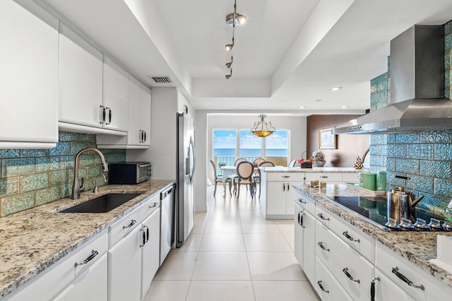 kitchen with sink, track lighting, white cabinetry, and wall chimney range hood