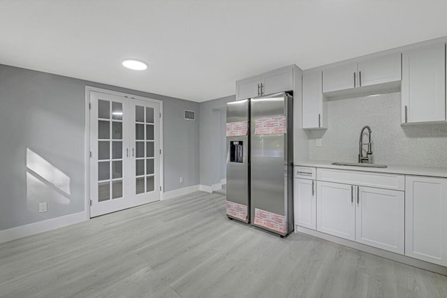 kitchen featuring sink, french doors, stainless steel fridge, decorative backsplash, and light wood-type flooring