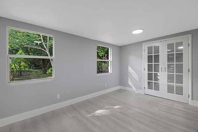 spare room featuring a healthy amount of sunlight, french doors, and light hardwood / wood-style floors