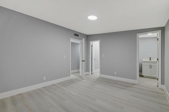 unfurnished bedroom featuring ensuite bathroom and light hardwood / wood-style flooring