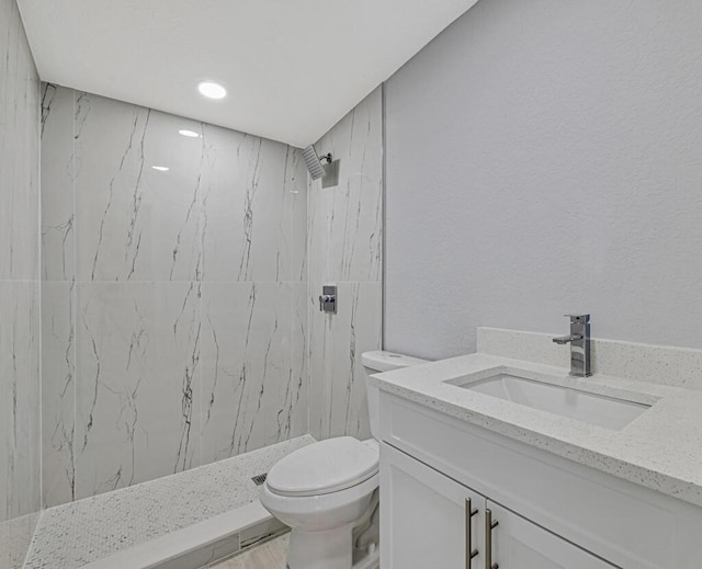 bathroom with a tile shower, vanity, and toilet