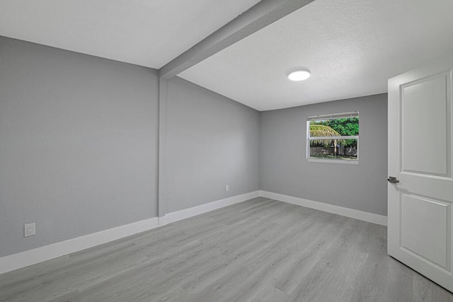 spare room with beamed ceiling, light hardwood / wood-style floors, and a textured ceiling