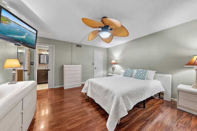 bedroom with ceiling fan, dark wood-type flooring, ensuite bathroom, and a textured ceiling