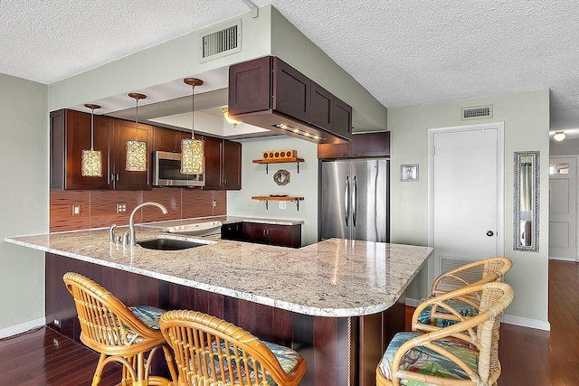 kitchen featuring sink, light stone countertops, decorative light fixtures, kitchen peninsula, and stainless steel appliances