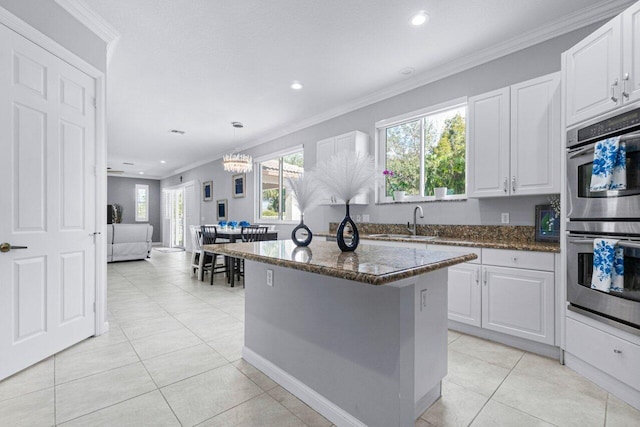 11158 Mainsail Ct, Wellington, FL 33449 - kitchen featuring stainless steel double oven, dark stone countertops, a center island, ornamental molding, and white cabinets