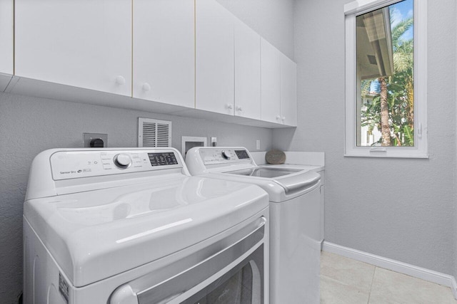 clothes washing area with washer and clothes dryer, light tile patterned flooring, cabinets, and a wealth of natural light