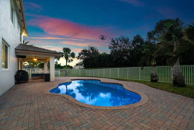 pool at dusk with a patio area and ceiling fan