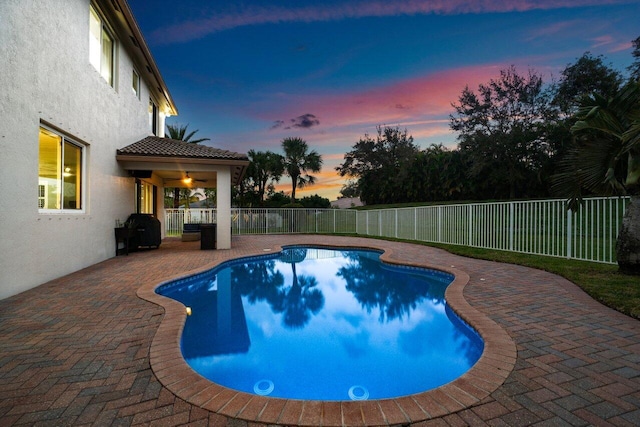 pool at dusk featuring a patio, ceiling fan, and grilling area