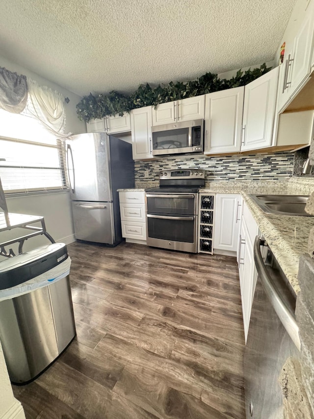 kitchen featuring white cabinetry, stainless steel appliances, light stone counters, dark hardwood / wood-style floors, and a textured ceiling