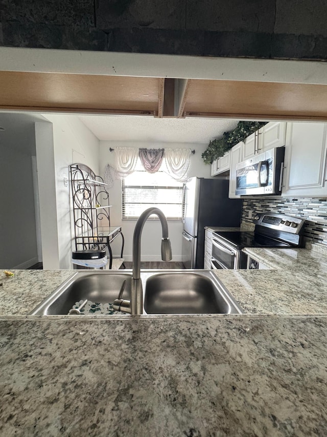 kitchen with backsplash, stainless steel appliances, white cabinetry, and sink