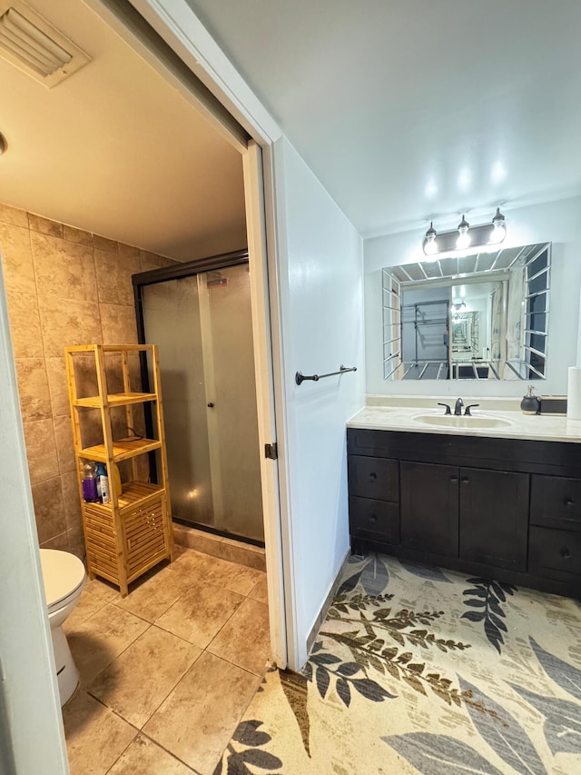 bathroom with vanity, a shower with door, tile walls, tile patterned flooring, and toilet