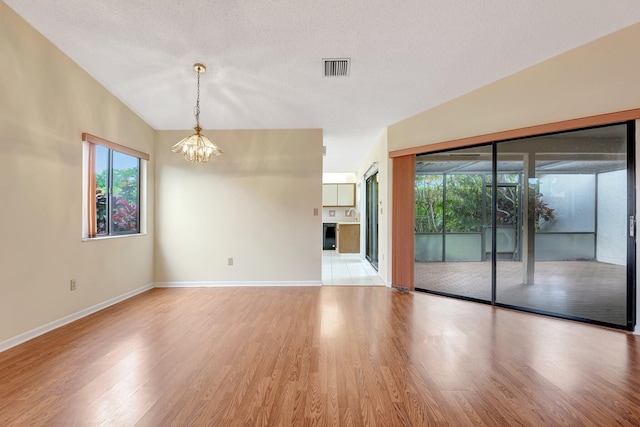 unfurnished room featuring lofted ceiling, a textured ceiling, light hardwood / wood-style floors, and a notable chandelier