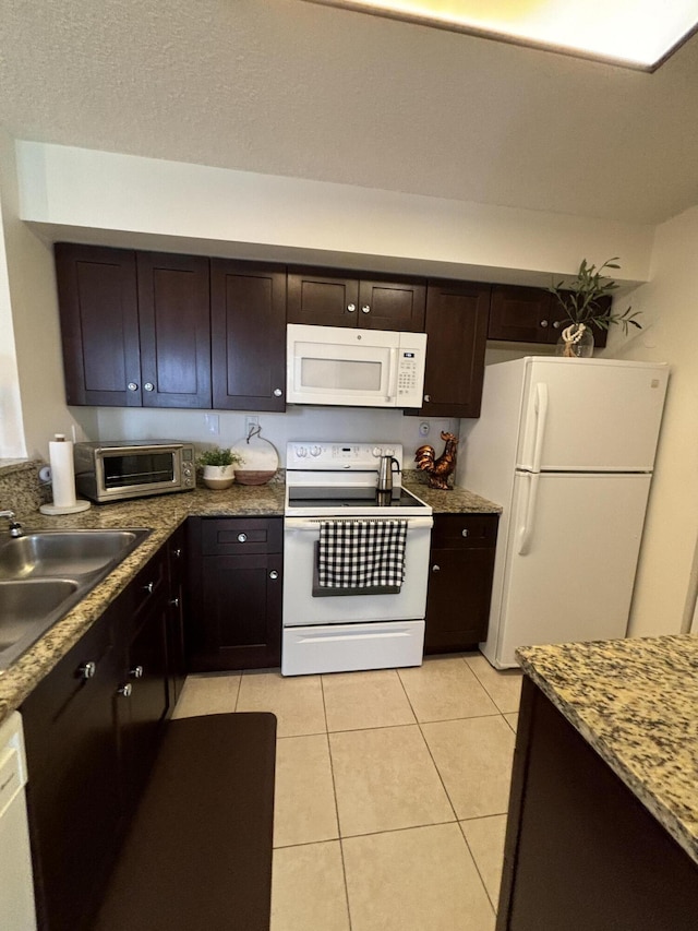 kitchen featuring dark brown cabinets, white appliances, sink, and light tile patterned floors