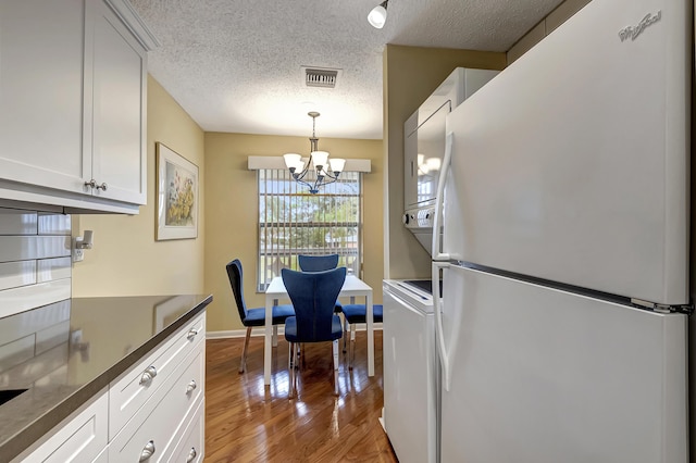 kitchen featuring white cabinetry, an inviting chandelier, white refrigerator, stacked washer / dryer, and decorative light fixtures