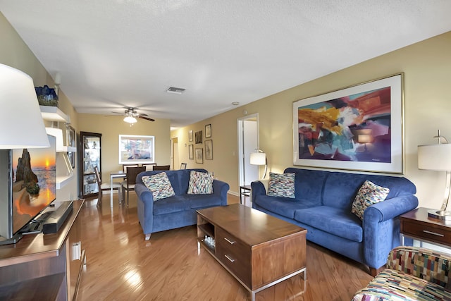 living room with ceiling fan, light hardwood / wood-style floors, and a textured ceiling