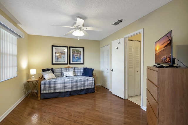 bedroom with two closets, ceiling fan, hardwood / wood-style floors, and a textured ceiling