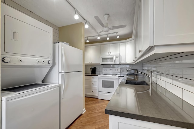 kitchen featuring white cabinetry, stacked washer and dryer, white appliances, and sink