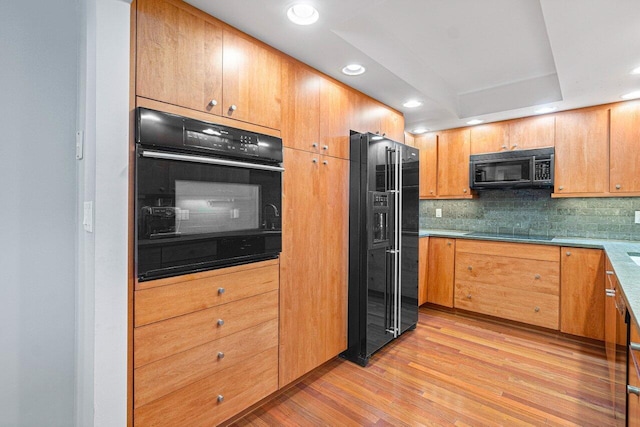 kitchen featuring decorative backsplash, light hardwood / wood-style floors, a tray ceiling, and black appliances