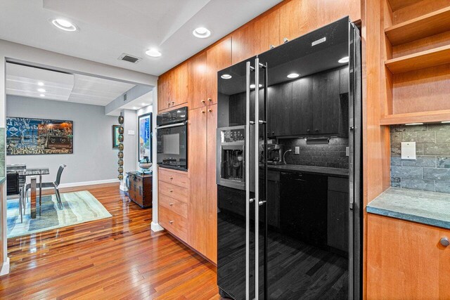 kitchen with black appliances, decorative backsplash, and light hardwood / wood-style flooring