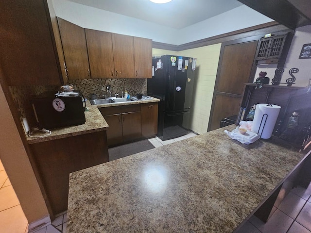 kitchen featuring black refrigerator, dark brown cabinets, backsplash, and light tile patterned floors