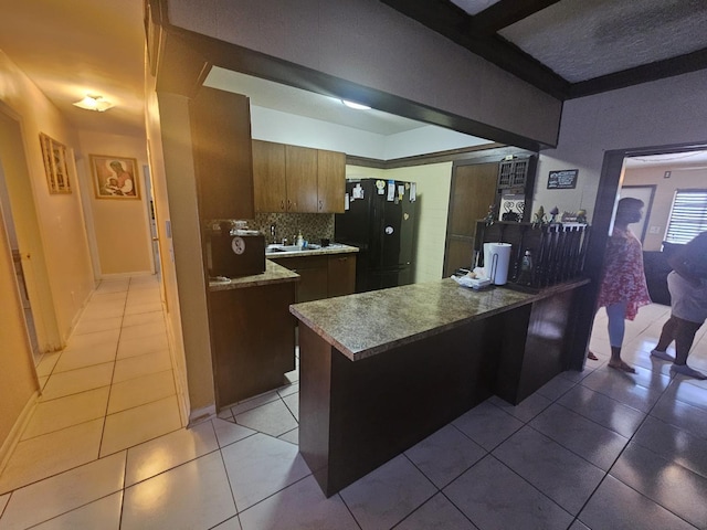 kitchen featuring a breakfast bar, backsplash, black refrigerator, light tile patterned floors, and kitchen peninsula