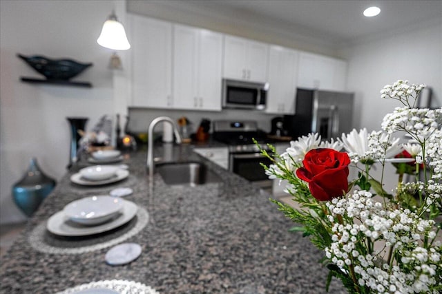 kitchen featuring sink, appliances with stainless steel finishes, dark stone counters, white cabinets, and ornamental molding