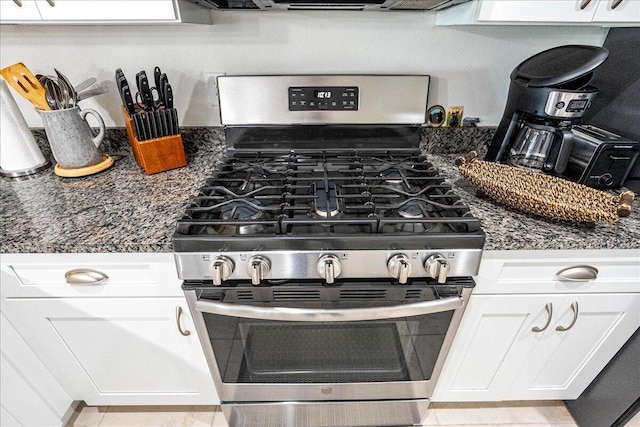 kitchen featuring stainless steel gas range oven, dark stone countertops, and white cabinetry