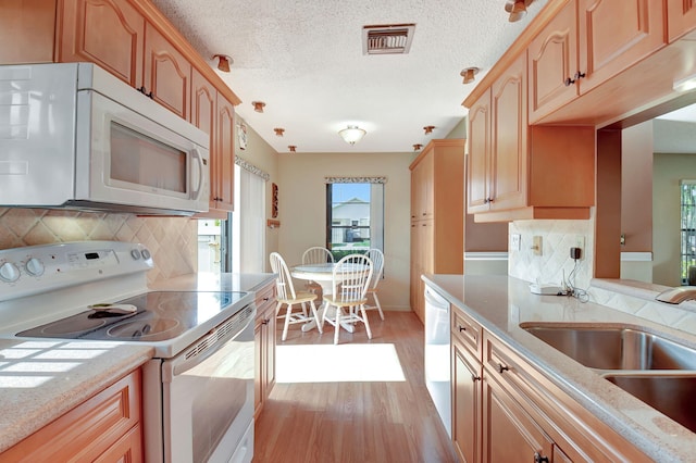 kitchen with backsplash, a textured ceiling, white appliances, sink, and light hardwood / wood-style floors