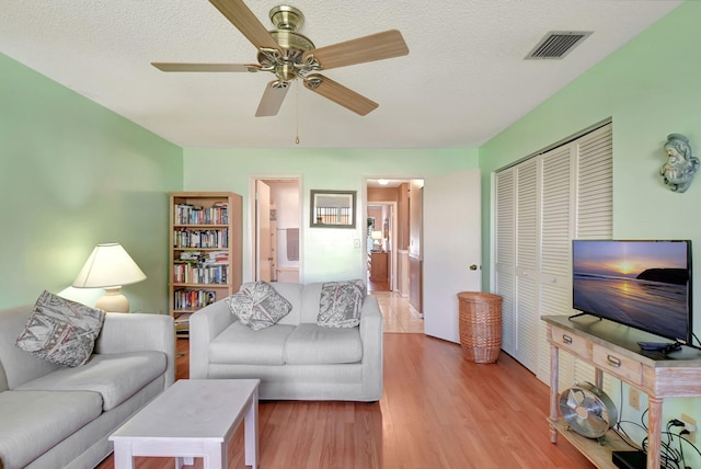 living room featuring ceiling fan, light hardwood / wood-style flooring, and a textured ceiling