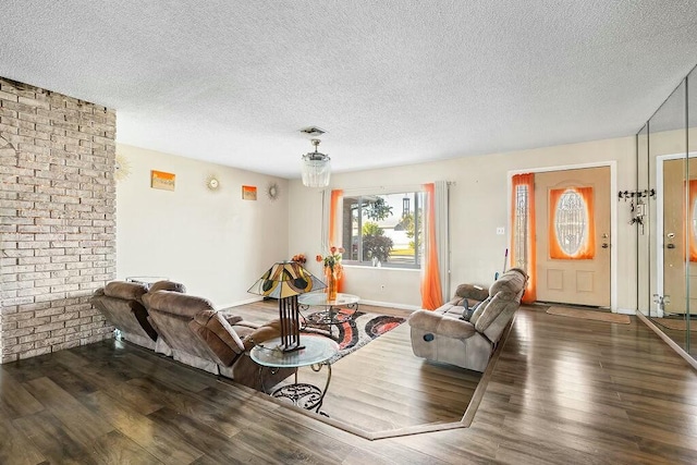 living room with a textured ceiling, dark wood-type flooring, and brick wall