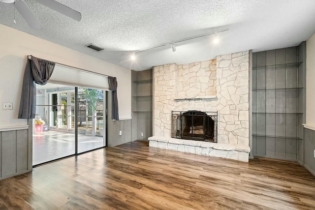 unfurnished living room featuring hardwood / wood-style floors, rail lighting, ceiling fan, a textured ceiling, and a fireplace