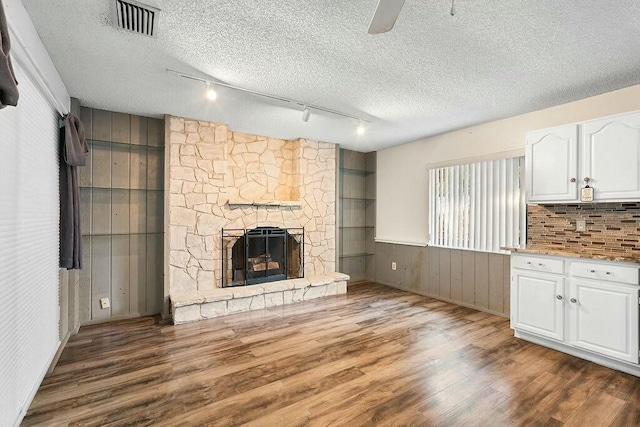 unfurnished living room with a textured ceiling, dark hardwood / wood-style floors, a stone fireplace, and ceiling fan