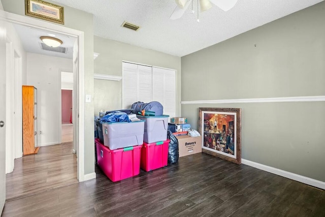 recreation room featuring a textured ceiling, ceiling fan, and dark wood-type flooring