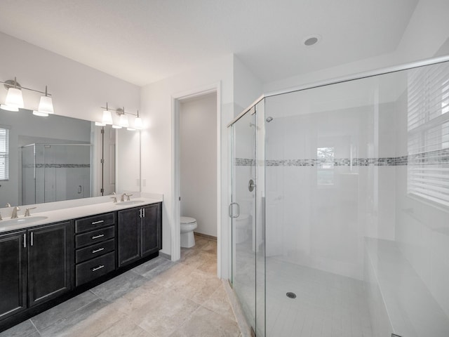 bathroom featuring a shower with door, toilet, vanity, and a healthy amount of sunlight